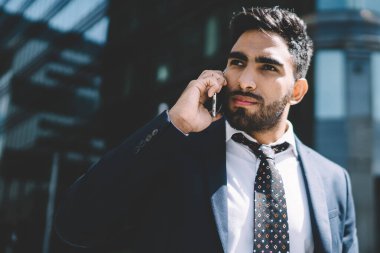 İspanyol sakallı adam iş seyahati sırasında patronla uluslararası konuşma yapmak için dolaşım bağlantısını kullanıyor, ciddi bir erkek girişimci akıllı telefondan operatöre başvuruyor.