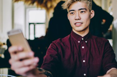 Japon hipster adam elinde cep telefonuyla tanıtım alanına bakıyor ve Çin 'li erkek blogcunun elinde modern akıllı telefon ile kablosuz bağlantısını bekliyor.