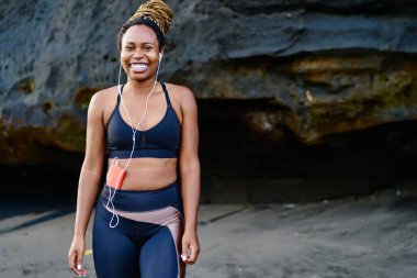 Kulaklıklı müzik uygulamasından ses şarkıları dinlerken kameraya gülümseyen mutlu afro amerikalı genç kadının portresi, spor eşofman giymiş neşeli koyu tenli koşucu heyecanlı