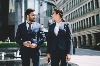 Multicultural male and female entrepreneurs walking around city street in downtown and communicate about upcoming startup project,diverse business people in formal suit strolling in financial district clipart