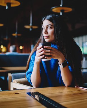 Düşünceli hipster kız kafede otururken ve kahve içerken kenara bakıyor, büyüleyici kadın 20 yaşında hayal ve ortak çalışma alanında boş yeniden oluştururken geleceği hakkında düşünme