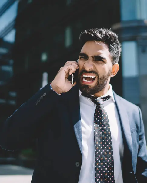 Öfkeli yetişkin erkek yönetmen, uluslararası arama sırasında kötü haber aldığı için kızgın. Akıllı telefon uygulaması ile konuşurken çalışana bağıran, suratında çılgın bir ifade olan adam.