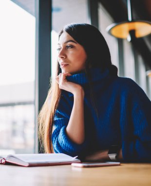 Güzel genç beyaz kadın model oturan ve kapalı boş zevk, çekici hipster kız 20 yaşında mavi kazak giyen rüya uzakta bakarken ve loft kafede otururken