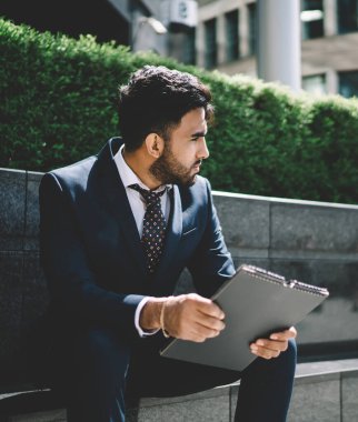 Düşünceli İspanyol erkek finans uzmanı resmi takım elbise giyip dışarıda oturuyor. Dosyada özgeçmişi var. Şirket yöneticisiyle görüşmeden önce düşünceli ve gergin hissediyorum.