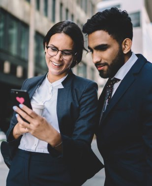 Başarılı, neşeli kadın girişimci finans web sitesinde, yanında duran İspanyol erkek ortağa yönetimle ilgili komik bir şaka yaparak metin gösteriyor.