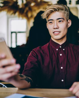 Japon hipster adam elinde cep telefonuyla tanıtım alanına bakıyor ve Çin 'li erkek blogcunun elinde modern akıllı telefon ile kablosuz bağlantısını bekliyor.