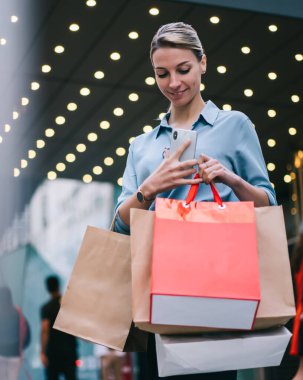 Kara Cuma günü alışveriş merkezinden alışveriş yaptıktan sonra elinde kağıt torbalarla gezen mutlu kadın, alışveriş saatinden sonra alışveriş yapan beyaz kadın, tanıtım alanında beklerken dinleniyor.