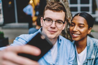 Birbirine aşık pozitif çok kültürlü çiftler sosyal ağlar için akıllı telefonlarda selfie çekiyorlar. Neşeli çeşitli arkadaşlar cep telefonlarıyla fotoğraf çekiyorlar.