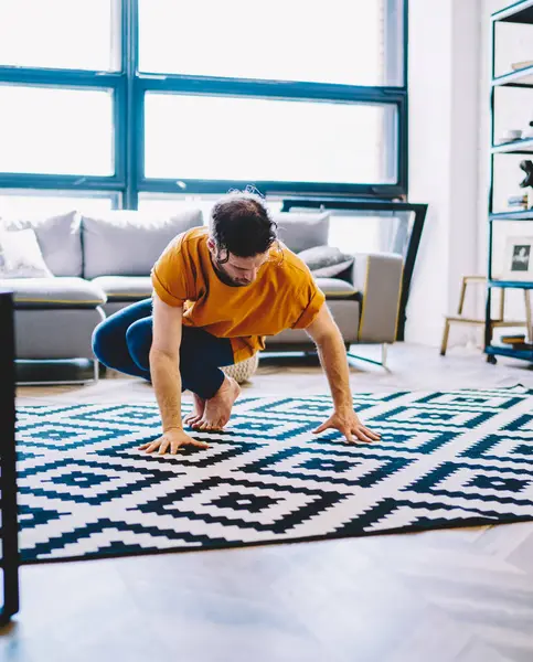 Young man dressed in active wear doing yoga exercises during morning training at home interior.Hipster guy practising relaxation during sportive training in modern apartment
