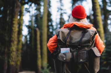 Moda turistik sırt çantalı, doğa ortamında duran ve gideceği yere giden yolu seçen genç bir gezginin arka görüntüsü. Dünya 'nın güzelliklerini keşfetmek için kadın yürüyüşçüler tatil yapıyor.