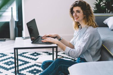 Modern dizüstü bilgisayarın uzaktan kumandasında, şık bir dairede ev internet bağlantısını kullanarak gülen olumlu genç bir kadın. Dairede oturmuş Netbook 'ta ders çalışan hippi kız.