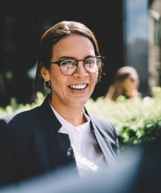 Optik gözlük takan neşeli, heyecanlı kadın girişimcilerin arka planda bakışları. Reklam alanında meslektaş şakasına gülmek, açık havada gülümseyen mutlu bir kadın.