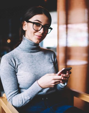 Gözlüklü neşeli blogcu portresi cep telefonuyla yeni yayın yaparken kameraya bakıyor, modern cep telefonu teknolojisini elinde tutan mutlu hippi kız dinleniyor.