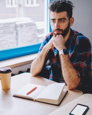 Ciddi sakallı hipster öğrenci dizüstü bilgisayar ile masaüstünde otururken düz görünümlü ve akademide ev ödevi düşünüyorum. Gündelik giyim genç adam eğitim ve üniversitede seminer için hazırlanıyor