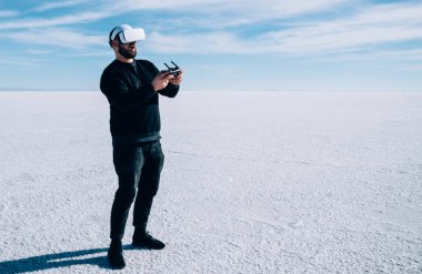 Gamepad 'li bir adam doğada VR kulaklık takarak sanal gerçeklik oyunu oynuyor. Hipster adam joystick bilgisayarıyla kontrol ediyor.