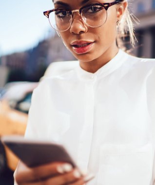 Finansal bölgede taksi çağırmak için mobil GPS uygulaması kullanırken kameraya bakan optik gözlüklü çekici genç kadının portresini kapat.