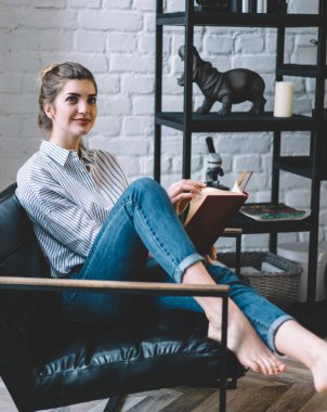 Düşünceli genç bir kadın, kitabının sayfasını çevirirken gülümsüyor modern bir dairede şık bir iç dekorasyonla koltukta oturuyor. Hippi kızın edebiyat okumaya boş vakitlerini ayırdığını düşünüyor.