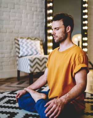Nilüfer çiçeğinde oturmuş, sabah evde meditasyon yaparken rahat bir şekilde poz veren genç sakin bir adam. Hippi her gün esneklik ve yaşayabilirliği desteklemek için yoga yapıyor.