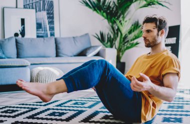Genç adam evde sağlıklı yaşam tarzını ve spor vücut şeklini destekleyen yoga egzersizleri yapıyor. Kaliteli iç dekorasyonla birlikte. Hippi adam sabah antrenmanı sırasında düz alanda meditasyon yapıyor.