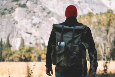 Aktif giyinmiş genç bir adam dağın yamacında dikiliyor ve doğanın güzel manzarasına hayran kalıyor. Tecrübeli bir erkek turist bahar tatili boyunca harika tepelerden keyif alıyor.