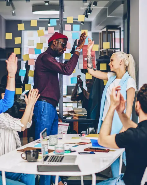 Happy african american leader of working team giving high five to female member celebrating success and great job, team of multiracial employees feeling happiness together during cooperation