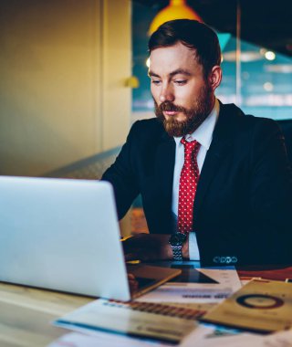 Resmi giyinmiş dalgın sakallı girişimci masaüstünde otururken modern dizüstü bilgisayarda iş webinar 'ı izliyor. Dijital netbook' ta çalışan konsantre erkek girişimci, e-posta yazıyor.