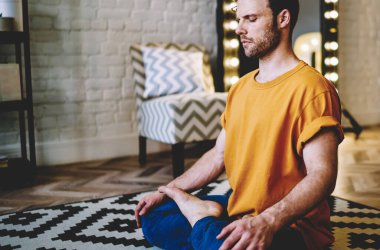 Nilüfer çiçeğinde oturmuş, sabah evde meditasyon yaparken rahat bir şekilde poz veren genç sakin bir adam. Hippi her gün esneklik ve yaşayabilirliği desteklemek için yoga yapıyor.