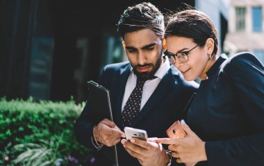 Çok kültürlü erkek ve kadın çalışanlar, açık havada internet taraması için akıllı telefondan 4G kablosuz bağlantıya geçen şirket çalışanları için yeni kamu başvurusu yoluyla iş arkadaşlarıyla iletişim kuruyor.