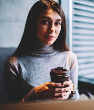 Çekici kız öğrenci coworking alanında dizüstü bilgisayar ile oturan kahve molası zevk kamera bakıyor, kafeteryada dinlenirken fincan ile poz kafkas güzel esmer kadın