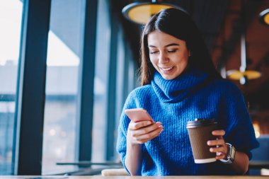 Kaygısız kadın hipster kız modern cep telefonu üzerinden arkadaşları ile sohbet ve kahve ile fincan tutarak, başarılı blogger iletişim ve cep telefonu numarası arama için uygulama yükleme