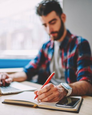 Modern dizüstü bilgisayar ve kablosuz 4G internetini kullanarak erkek eli kalem tutma ve web sitesinden metin bilgileri yazma üzerine seçici odaklan. Hipster öğrencisi netbook 'ta çalışırken notlar alıyor.