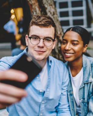 Birbirine aşık pozitif çok kültürlü çiftler sosyal ağlar için akıllı telefonlarda selfie çekiyorlar. Neşeli çeşitli arkadaşlar cep telefonlarıyla fotoğraf çekiyorlar.