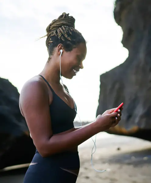 Happy afro american sportive woman choosing audio songs in music application on smartphone for morning run, dark skinned female in tracksuit listening player downloaded on mobile phone device