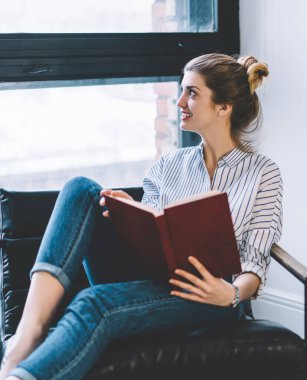 Ders kitabını elinde tutan, pencereden dışarı bakan, evinde oturan düşünceli, düşünceli genç bir kadın. Çok satanlar listesindeki ilginç edebiyat entrikalarını düşünen neşeli, düşünceli bir hippi kız.