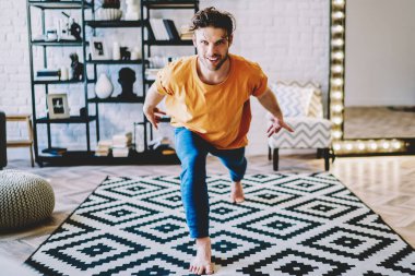 Evde yoga eğitimi sırasında kameraya gülümseyen genç bir adamın portresi. Modern apartmandaki meditasyondan önce motivasyonlu hipster çocuk ısınıyor.