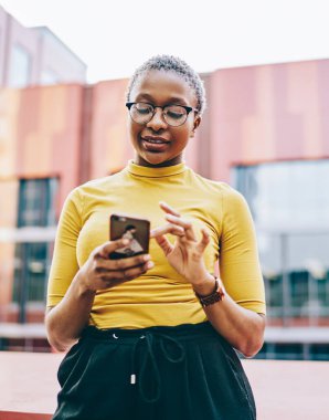 Neşeli koyu tenli genç kadın internet sitesinden alışveriş yapıyor modern akıllı telefondan şehir ortamında ücretsiz internet bağlantısı kullanıyor. Afro-Amerikan bayan antrenör mesajını aldı.