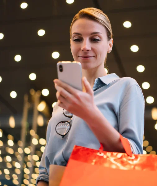 Consumerism and youth lifestyle concept, positive young woman holding colorful shopping bags and modern smartphone device for checking sales and prices in favourite stores during Black Friday