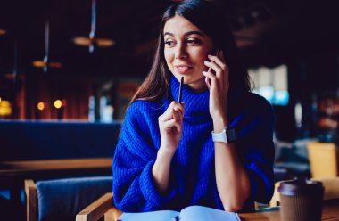 Kafeteryada dinlenirken modern akıllı telefon aracılığıyla arkadaşıyla olumlu sohbet eden neşeli hipster kız, kapalı mekanlarda 4g internet ile telefonla uygulama kullanarak arayan başarılı bir kadın