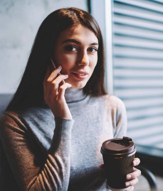 Olumlu kız öğrenci portresi dinlenme ve kahve içerken akıllı telefon uygulaması üzerinden arkadaşı ile iletişim, kaygısız kadın konuşma ve kamera bakarak telefon kullanarak