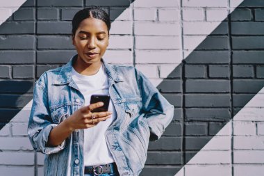 Gündelik kot giyen Afrikalı Amerikalı genç bir kadın elinde akıllı telefon ve sosyal ağlarda internetten 4G internet kullanarak sohbet ediyor. Çevrimiçi bankacılık cep telefonunda. Uygulamada mesaj gönderiliyor