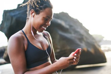 Neşeli koyu tenli kadın sportif giyim okuma giymiş online müzik dinlemek için akıllı telefon gadget 4g kablosuz kullanarak açık havada koşu mola sırasında arkadaşından komik e-posta aldı