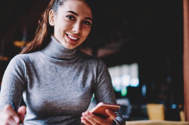 Beyaz başarılı kadın e-posta uygulaması ve 4g internet ile cep telefonu kullanarak gülümseyerek ve kamera bakarken, bağlı mutlu bin yıllık hipster kız kapalı teknoloji kavramı