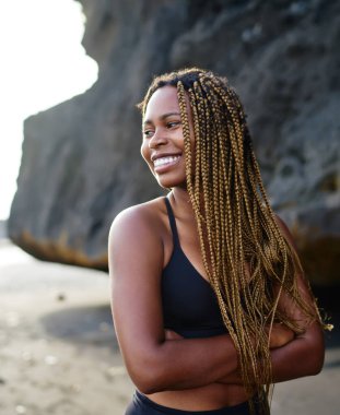 Neşeli koyu tenli sportwoman aktif giysiler kayalar yakınında gülümseyen giymiş, heyecansportif afro amerikan genç kız zayıflama için sabah kardiyo egzersiz önce açık havada şık üst ayakta