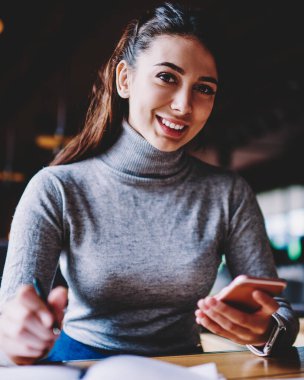 Beyaz başarılı kadın e-posta uygulaması ve 4g internet ile cep telefonu kullanarak gülümseyerek ve kamera bakarken, bağlı mutlu bin yıllık hipster kız kapalı teknoloji kavramı