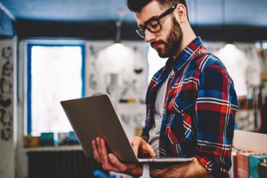 Sakallı hipster adam dizüstü bilgisayar tutan ve kütüphane iç ücretsiz kablosuz internet kullanarak cihaz da yazılım güncelleme. Genç adam öğrenci dijital netbook web sitesinde veri arıyor