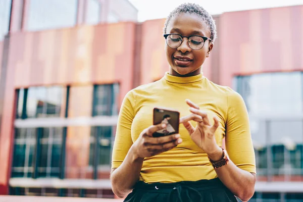 Neşeli koyu tenli genç kadın internet sitesinden alışveriş yapıyor modern akıllı telefondan şehir ortamında ücretsiz internet bağlantısı kullanıyor. Afro-Amerikan bayan antrenör mesajını aldı.