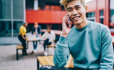 Açık havada gülümseyen ve konuşan neşeli Japon hippi. Şık giyinmiş Çinli genç adam cep telefonundan arıyor ve arkadaşlarıyla iletişim kuruyor.