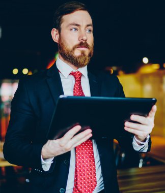 Resmi giyinmiş deneyimli beyaz girişimci ofis içi ayakta dururken modern dokunmatik ped yazılımını güncellerken gözlerini kaçırıyor. Tablette çevrimiçi bankacılık programı kullanılıyor