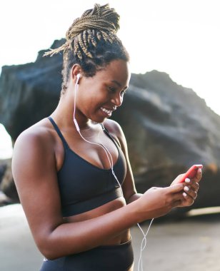 Neşeli koyu tenli kadın sportif giyim okuma giymiş online müzik dinlemek için akıllı telefon gadget 4g kablosuz kullanarak açık havada koşu mola sırasında arkadaşından komik e-posta aldı