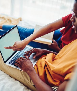 Genç Afro-Amerikan evliliğinin internetten alışveriş için dizüstü bilgisayarla internete bağlanan görüntüsü. Aşıklar internet üzerinden rezervasyon yapıyor ve fikirleri tartışıyorlar.